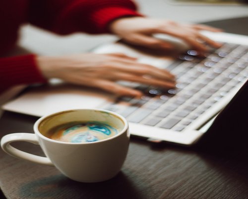 Detalle de manos en el teclado y taza de café